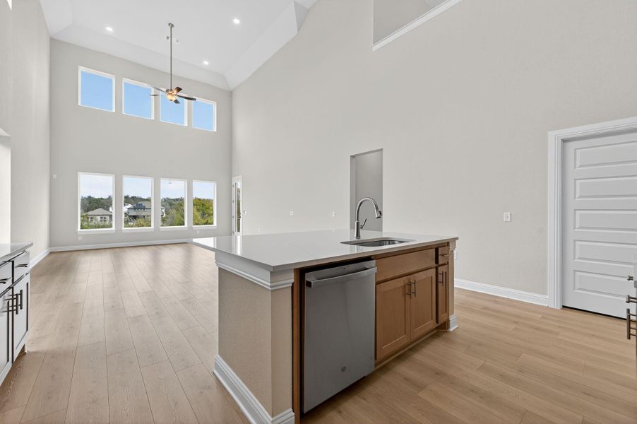 Kitchen with a kitchen island with sink, dishwasher, open floor plan, brown cabinetry, and light wood-style floors