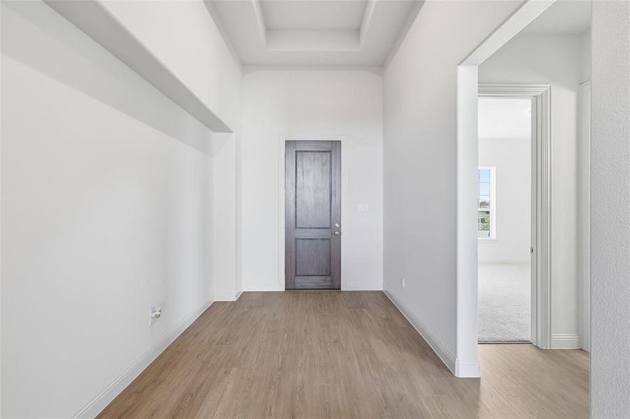 Hall featuring light wood-type flooring and a raised ceiling Hall featuring light wood-type flooring and a raised ceiling