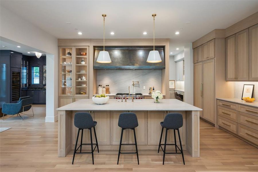 Kitchen with a spacious island, a kitchen bar, ventilation hood, and light wood-type flooring