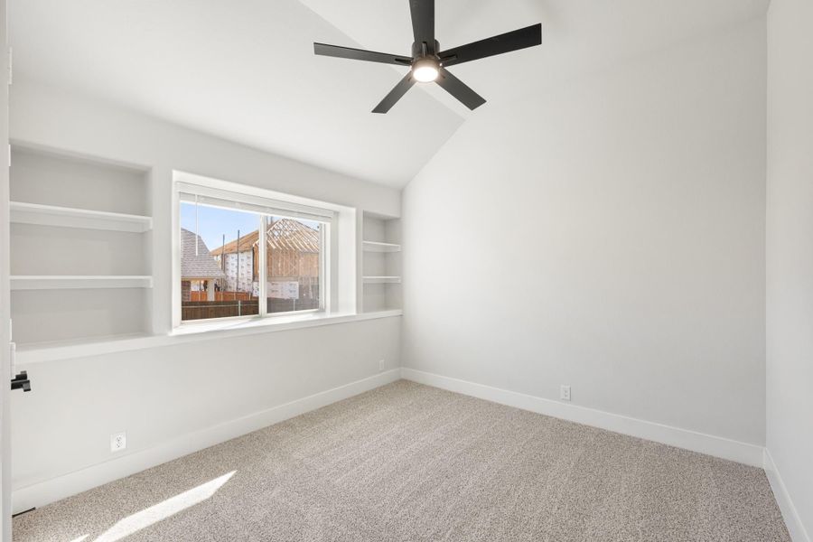 Empty bedroom with vaulted ceiling, black ceiling fan, built-in shelves, and carpet flooring