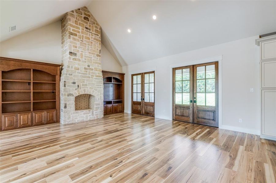 Unfurnished living room featuring high vaulted ceiling, a fireplace, french doors, and built in cabinets