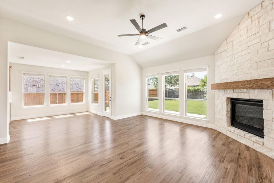 Open living room with hardwood floors, stone fireplace, ceiling fan, and large windows overlooking backyard Open living room with hardwood floors, stone fireplace, ceiling fan, and large windows overlooking backyard