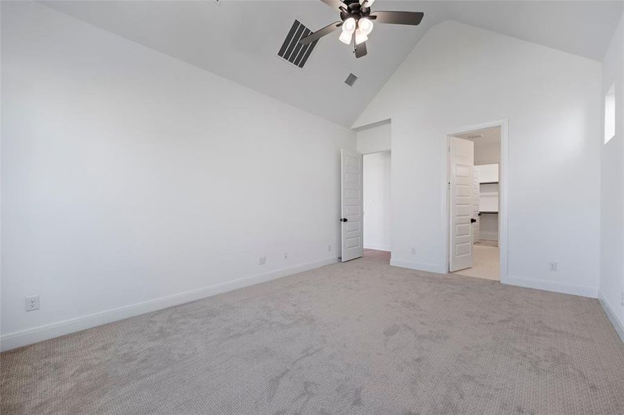 Unfurnished bedroom featuring a walk in closet, high vaulted ceiling, ensuite bathroom, ceiling fan, and light colored carpet