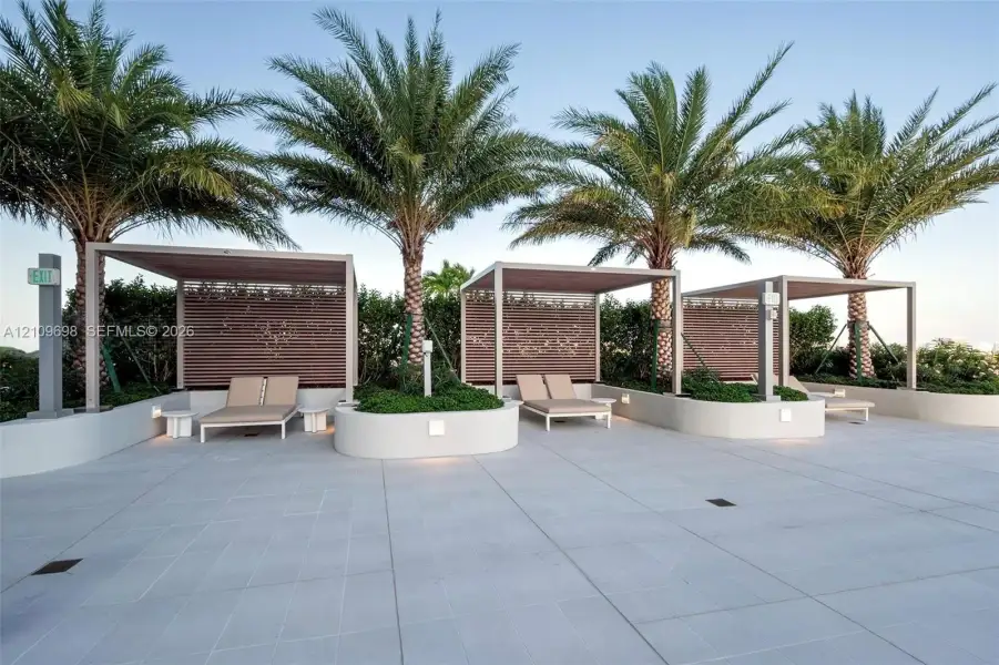 Outdoor terrace featuring large-format paver tiles, built-in curved concrete planters, structural shade pergolas, and integrated privacy screens