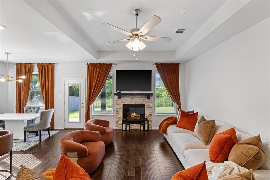 Spacious living area featuring rich wood-finish flooring, a stone-clad fireplace with a dark mantel, and recessed ceiling lighting