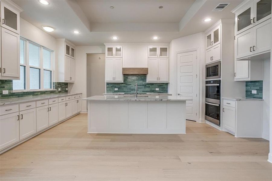 Kitchen featuring white cabinetry, a tray ceiling, decorative backsplash, and an island with sink