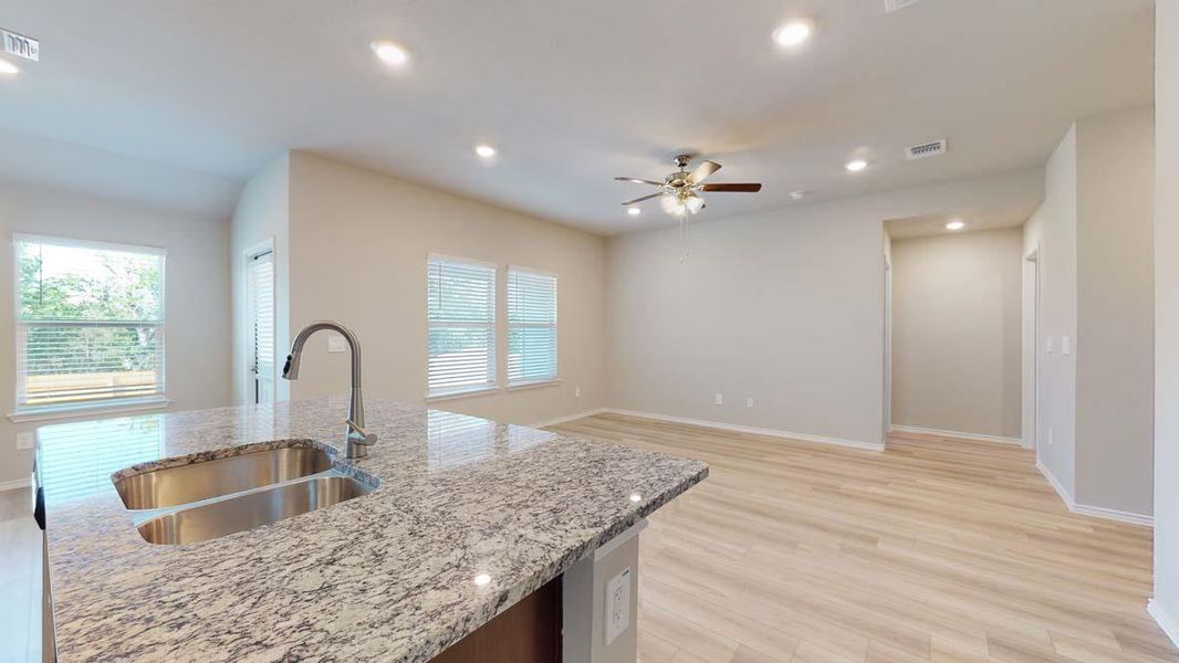 Kitchen island featuring a double basin stainless steel sink with gooseneck faucet, light-toned granite-style countertop, and recessed lighting