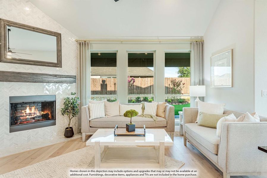 Living room with vaulted ceiling, tile fireplace, neutral sofas, and large windows overlooking backyard
