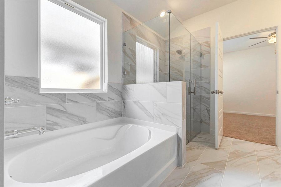 Primary bath featuring a soaking tub, separate glass-enclosed shower, marble-look tile surround, and natural light from the privacy window. The layout creates a bright and relaxing retreat with clean modern finishes.