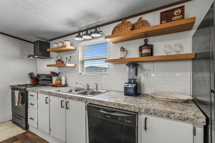 Kitchen featuring backsplash, black appliances, a textured ceiling, wall chimney range hood, and white cabinets