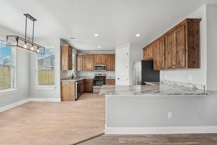 Kitchen with brown cabinets, light wood-style flooring, a sink, appliances with stainless steel finishes, and a peninsula