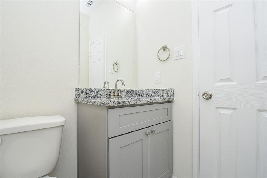 A small bathroom with a toilet, granite countertop sink, and white doors. Clean, modern, and minimalistic design.