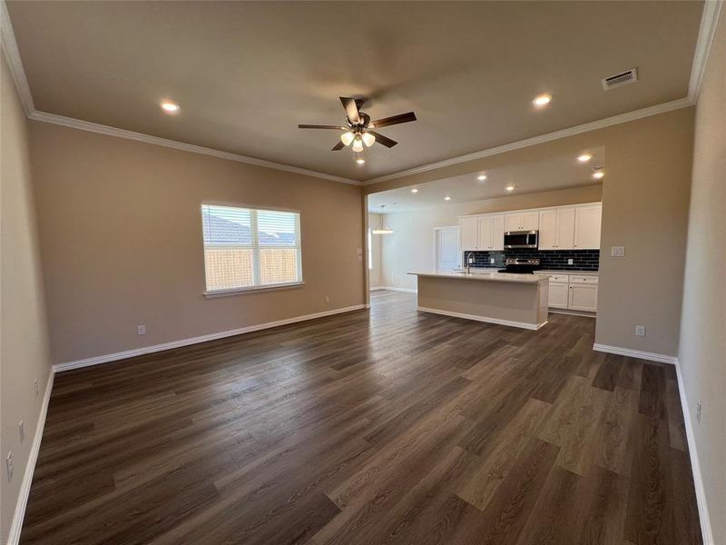 Unfurnished living room with crown molding, ceiling fan, and dark wood-type flooring