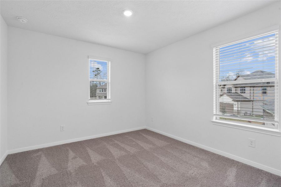 This secondary bedroom offers comfort and style with plush carpeting, neutral paint tones, recessed lighting, windows with blinds, and a generously sized closet.