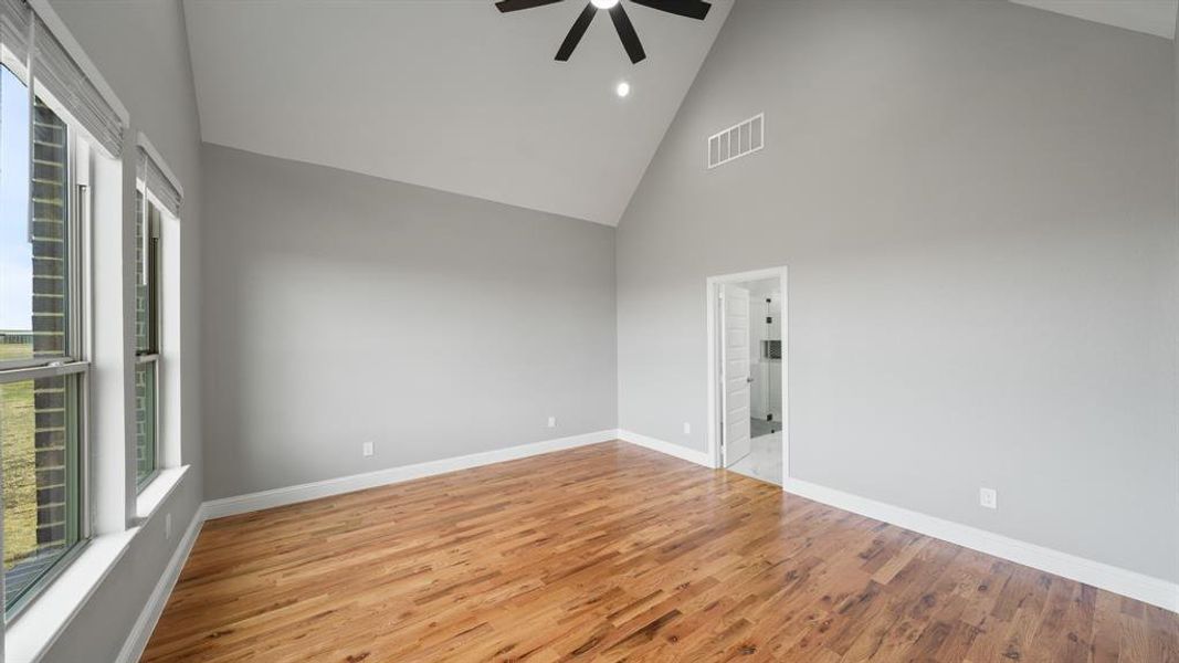 Empty room with baseboards, visible vents, ceiling fan, wood finished floors, and high vaulted ceiling