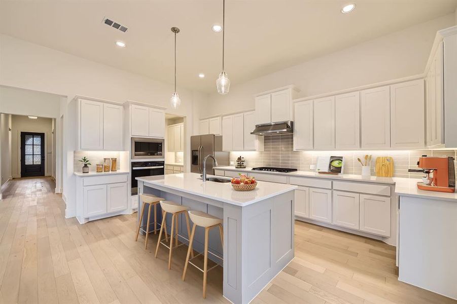 Virtually Staged - Kitchen with tasteful backsplash, light wood finished floors, recessed lighting, a center island with sink, and a kitchen breakfast bar