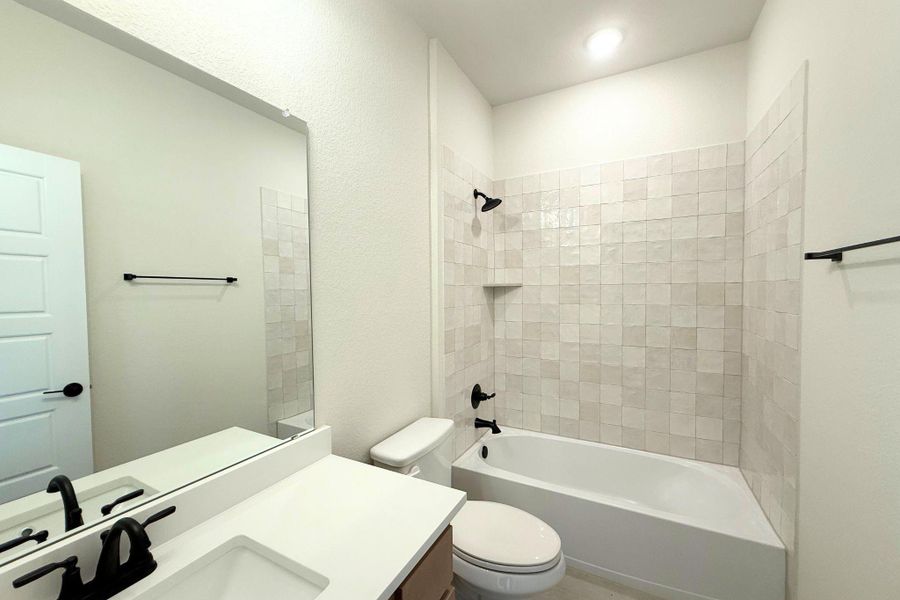 A pristine full bathroom, featuring a clean white vanity, a large mirror, and a bathtub with tiled surround. A pristine full bathroom, featuring a clean white vanity, a large mirror, and a bathtub with tiled surround.