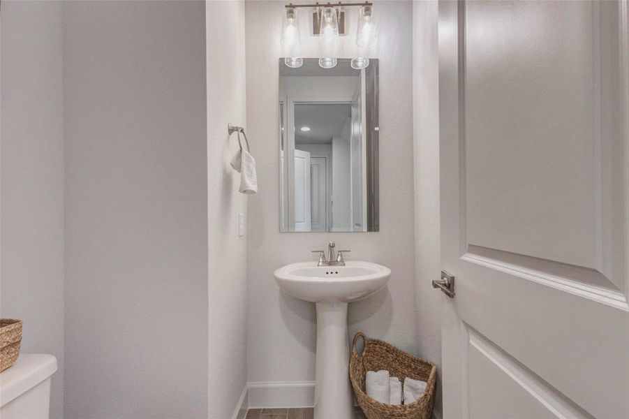 This is a compact, modern powder room featuring a pedestal sink, a large mirror, and stylish lighting. The neutral tones and clean design offer a fresh, inviting feel. This is a compact, modern powder room featuring a pedestal sink, a large mirror, and stylish lighting. The neutral tones and clean design offer a fresh, inviting feel.