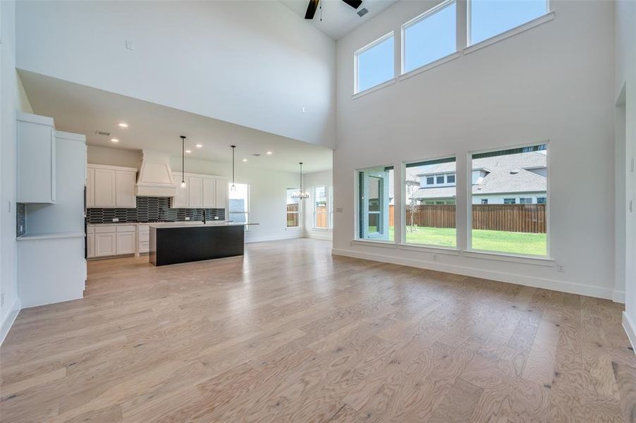 Unfurnished living room featuring sink, light wood-type flooring, and a towering ceiling