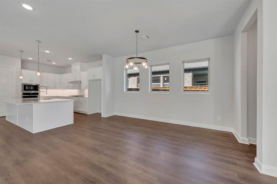 Kitchen with white cabinetry, hanging lights, a center island with sink, dark wood-type flooring, and stainless steel appliances