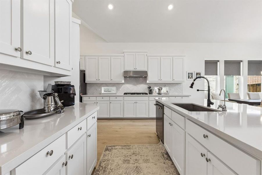 Bright kitchen featuring white shaker cabinetry, light countertops, wood-finish flooring, a center island with sink, and a stainless steel appliance suite