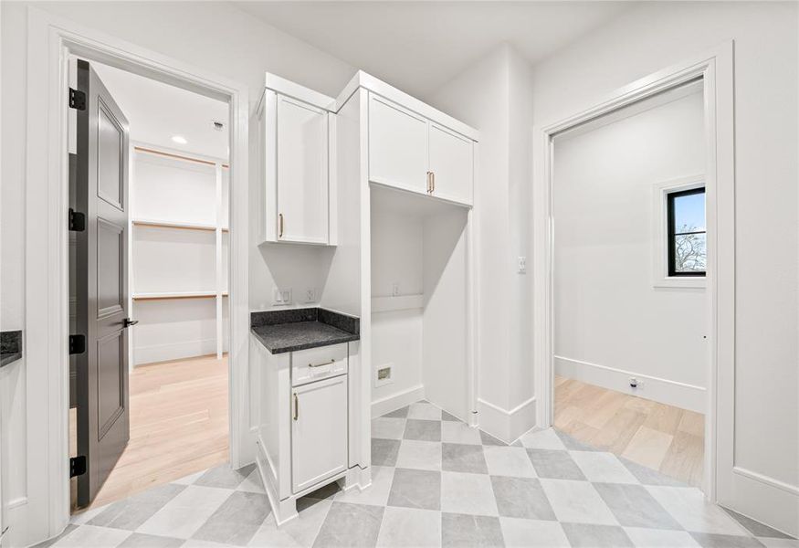 Utility area with checkerboard tile flooring, built-in white cabinetry, dark stone countertops, and gold-finish hardware