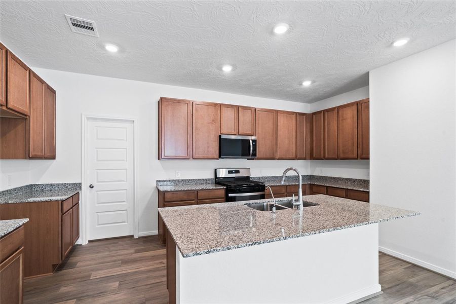 The central kitchen island features a durable granite countertop and an undermount stainless steel sink with a Moen faucet. The kitchen island has additional storage space, increased counter and prep space, and is the social hub of the home--where family and guests gather and interact!