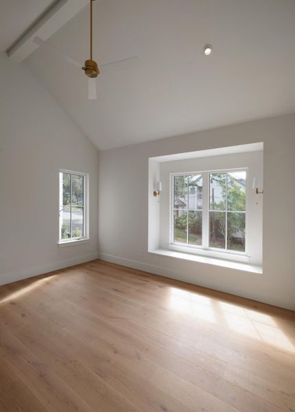 Large primary bedroom features vaulted ceilings, white oak flooring, bench nook with designer sconces.