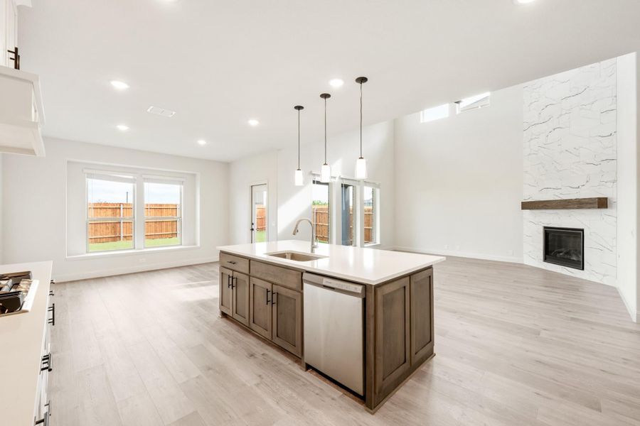 Open kitchen with dark wood island, pendant lights, and stone fireplace in adjoining living area Open kitchen with dark wood island, pendant lights, and stone fireplace in adjoining living area