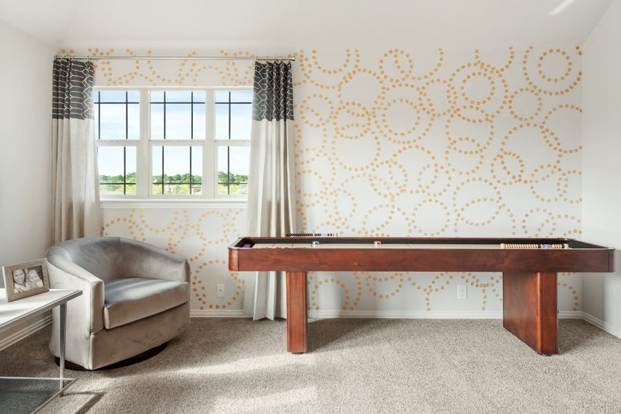 Game room with wood shuffleboard table, accent wall with dot pattern, and gray armchair on carpet