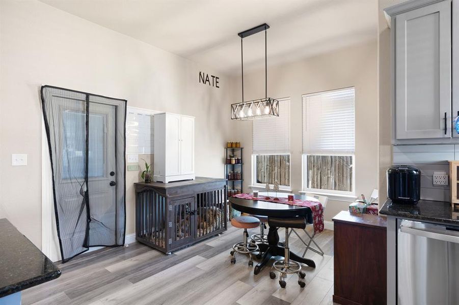 Kitchen with stainless steel dishwasher, light hardwood / wood-style floors, dark stone countertops, gray cabinets, and hanging light fixtures