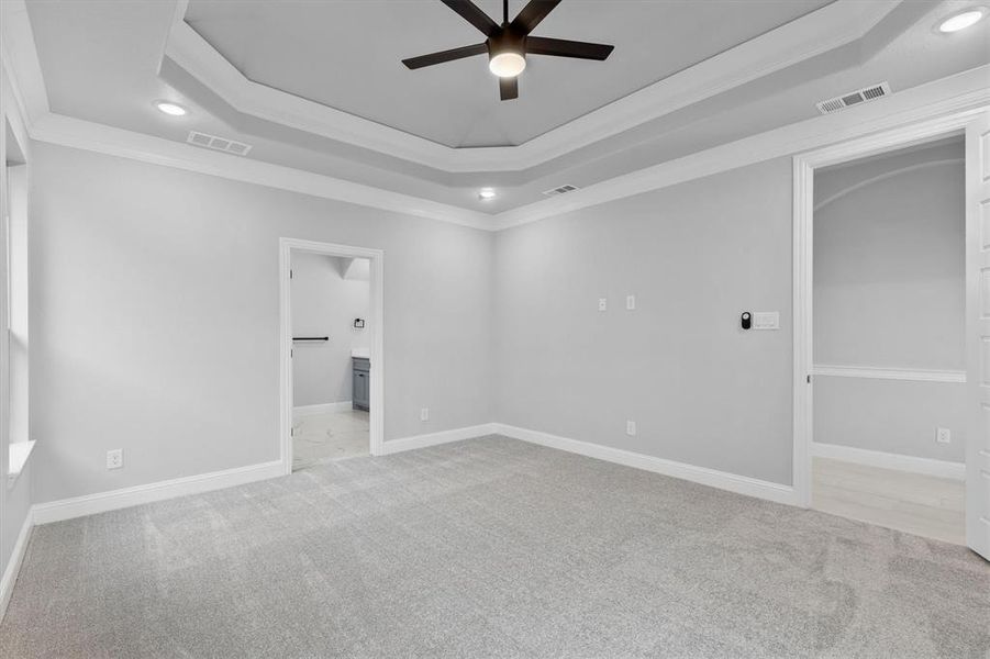 Unfurnished bedroom with connected bathroom, a tray ceiling, crown molding, light colored carpet, and ceiling fan