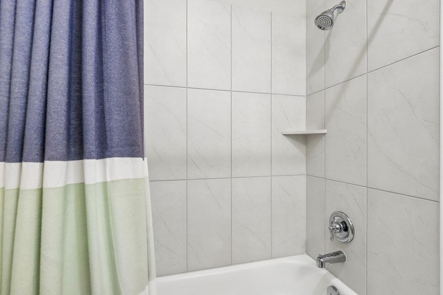 A well-appointed bath features a tiled shower with a built-in corner shelf and polished chrome fixtures.