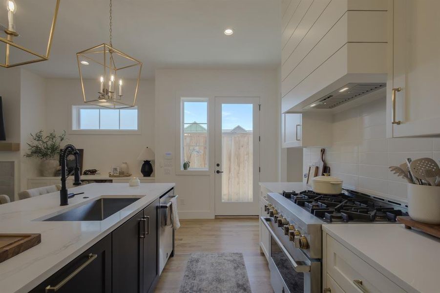 Kitchen with light stone countertops, sink, stainless steel appliances, decorative light fixtures, and white cabinets