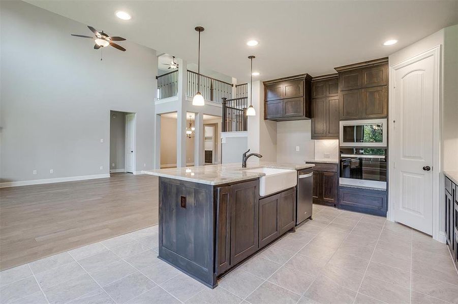 Kitchen with appliances with stainless steel finishes, a towering ceiling, dark brown cabinetry, and an island with sink