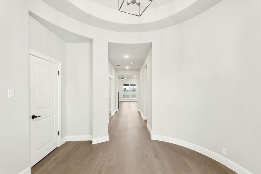 Curved foyer with tray ceiling, pendant light, hardwood floors, and hallway leading to main living area Curved foyer with tray ceiling, pendant light, hardwood floors, and hallway leading to main living area