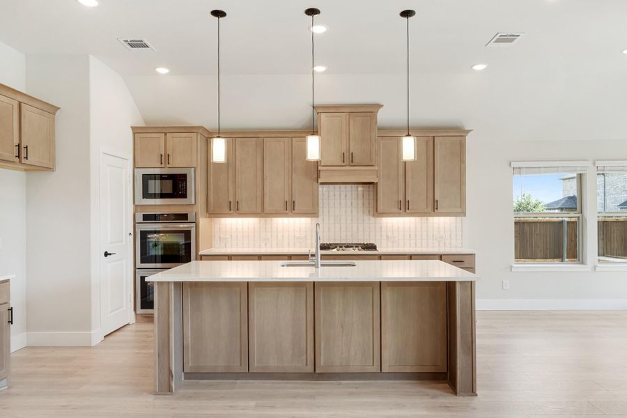 Kitchen with large center island, light wood cabinets, pendant lights, and stainless steel double oven