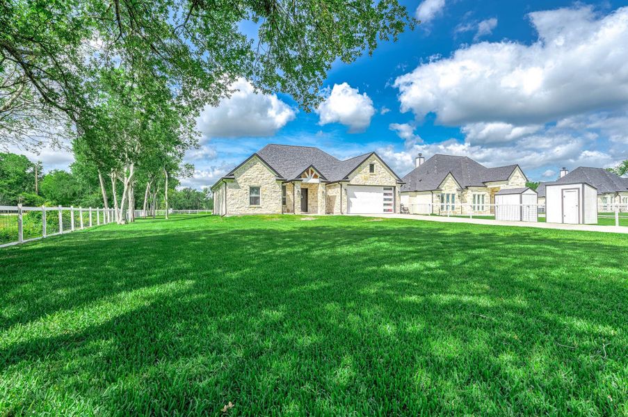 This spacious stone home is set against a backdrop of mature trees and features a beautifully maintained lawn with fenced outdoor space. The combination of modern design and natural surroundings creates a peaceful and inviting setting.