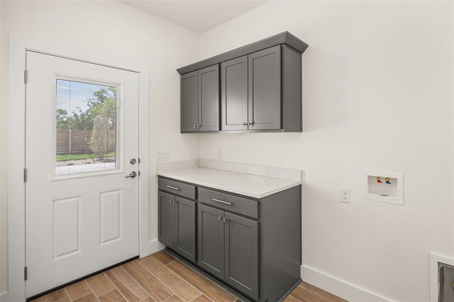 Laundry area featuring wood-finish tile flooring, a white paneled door with a window, and grey cabinetry with a light-colored countertop