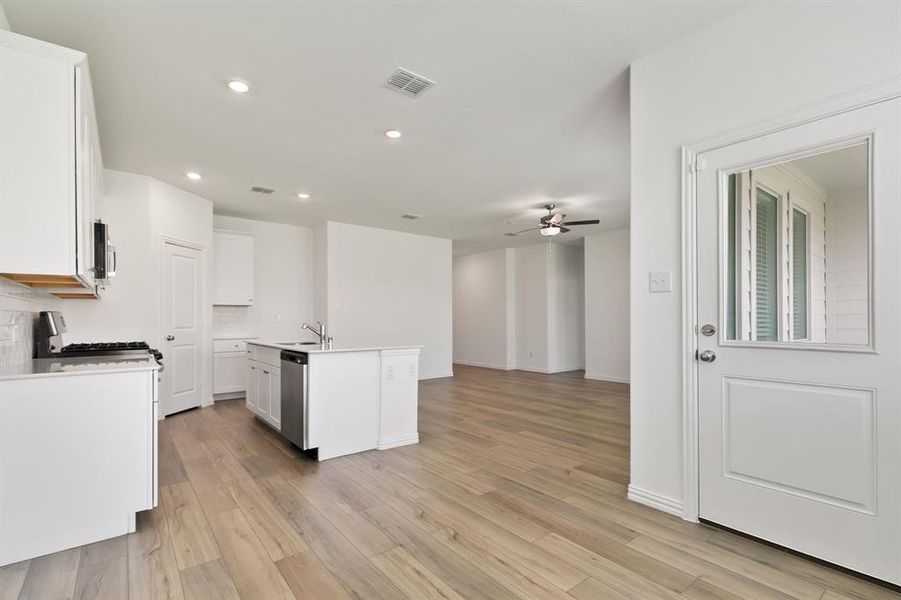 Kitchen with tasteful backsplash, light hardwood / wood-style flooring, ceiling fan, and a center island with sink