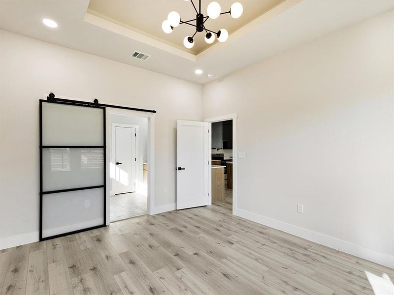Unfurnished bedroom featuring a chandelier, a barn door, recessed lighting, light wood finished floors, and a raised ceiling