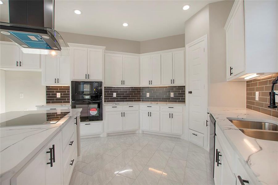 Kitchen featuring sink, white cabinetry, light stone counters, island exhaust hood, and black appliances