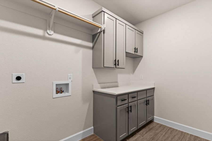 Washroom with dark wood finished floors, washer hookup, electric dryer hookup, cabinet space, and a textured wall Washroom with dark wood finished floors, washer hookup, electric dryer hookup, cabinet space, and a textured wall