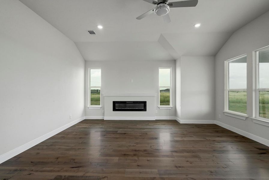 Unfurnished living room with vaulted ceiling, healthy amount of natural light, dark wood-style flooring, a glass covered fireplace, and recessed lighting