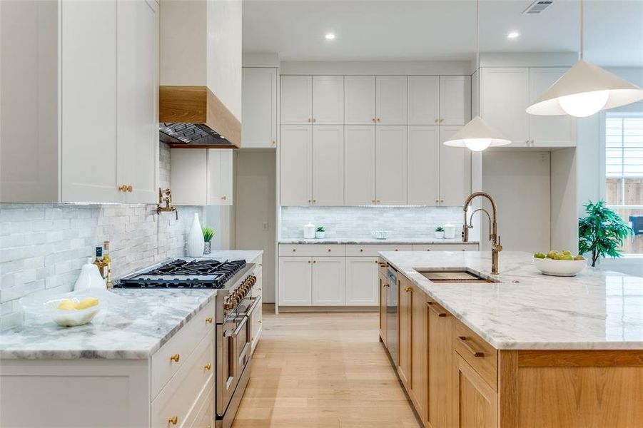 Kitchen with appliances with stainless steel finishes, custom range hood, white cabinets, and decorative light fixtures