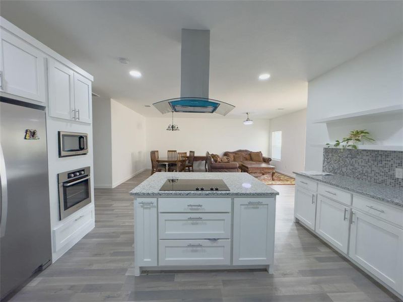 Kitchen with white cabinets, light style flooring, backsplash, island range hood, and appliances with stainless steel finishes