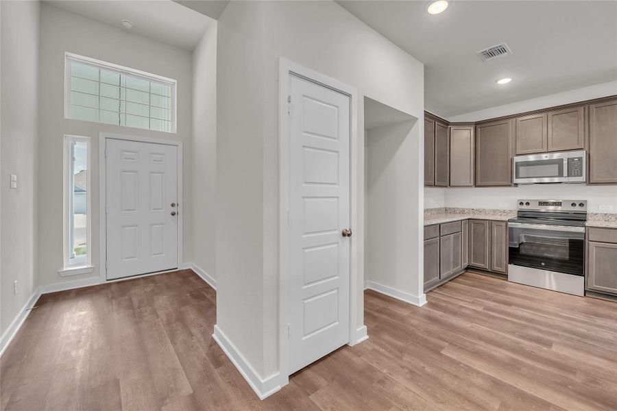 Kitchen featuring appliances with stainless steel finishes, light wood-type flooring, light stone countertops, recessed lighting, and dark brown cabinets Kitchen featuring appliances with stainless steel finishes, light wood-type flooring, light stone countertops, recessed lighting, and dark brown cabinets