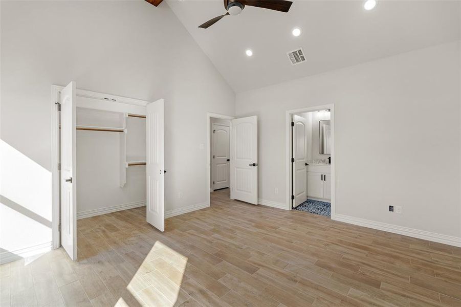 Unfurnished bedroom with ensuite bathroom, ceiling fan, light hardwood / wood-style flooring, high vaulted ceiling, and a closet