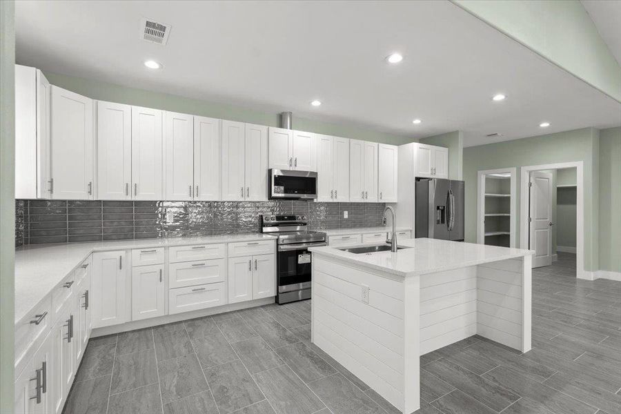Kitchen with appliances with stainless steel finishes, white cabinetry, light stone countertops, an island with sink, and recessed lighting