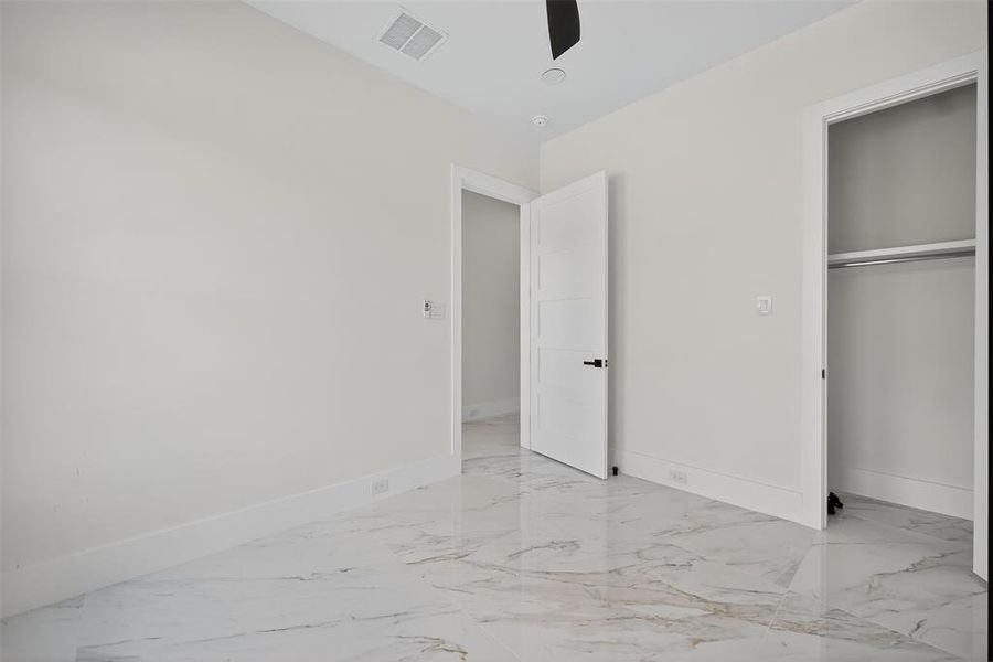 Unfurnished bedroom with light marble finish floors, ceiling fan, and a closet